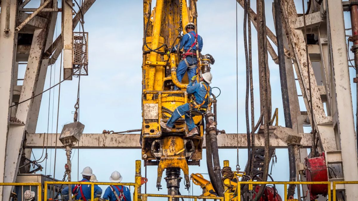 Drill crew in safety harnesses working on the top drive of a drilling rig derrick