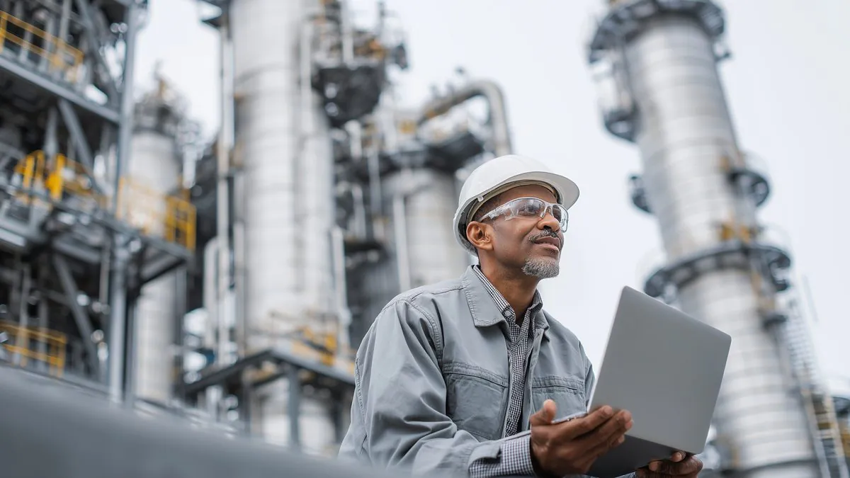 An engineer reviewing production data on a laptop in front of a gas processing plant